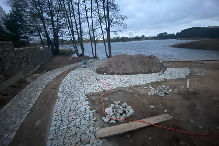 Układanie ścieżki z kostki granitowej nad brzegiem jeziora – prace brukarskie w terenie zielonym