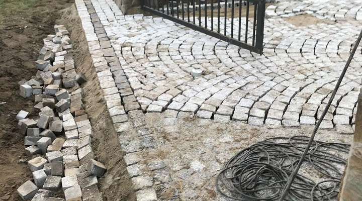 Układanie łukowego wzoru z kostki granitowej przy bramie wjazdowej – prace brukarskie w toku
